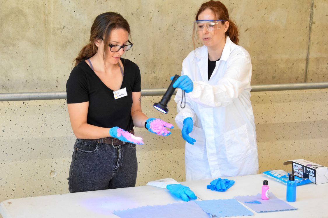 Beim Experiment mit Schwarzlicht zeigte Laura Dormann (LD-safety GmbH, rechts), wie leicht beim falschen Ausziehen eines Handschuhs Chemikalien auf die Haut gelangen können. (Bild: BUL, zVg)