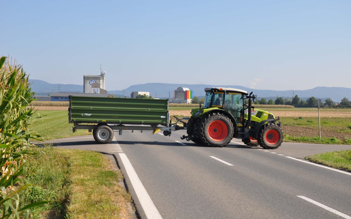 Ein grüner Traktor mit Anhänger überquert eine Strasse